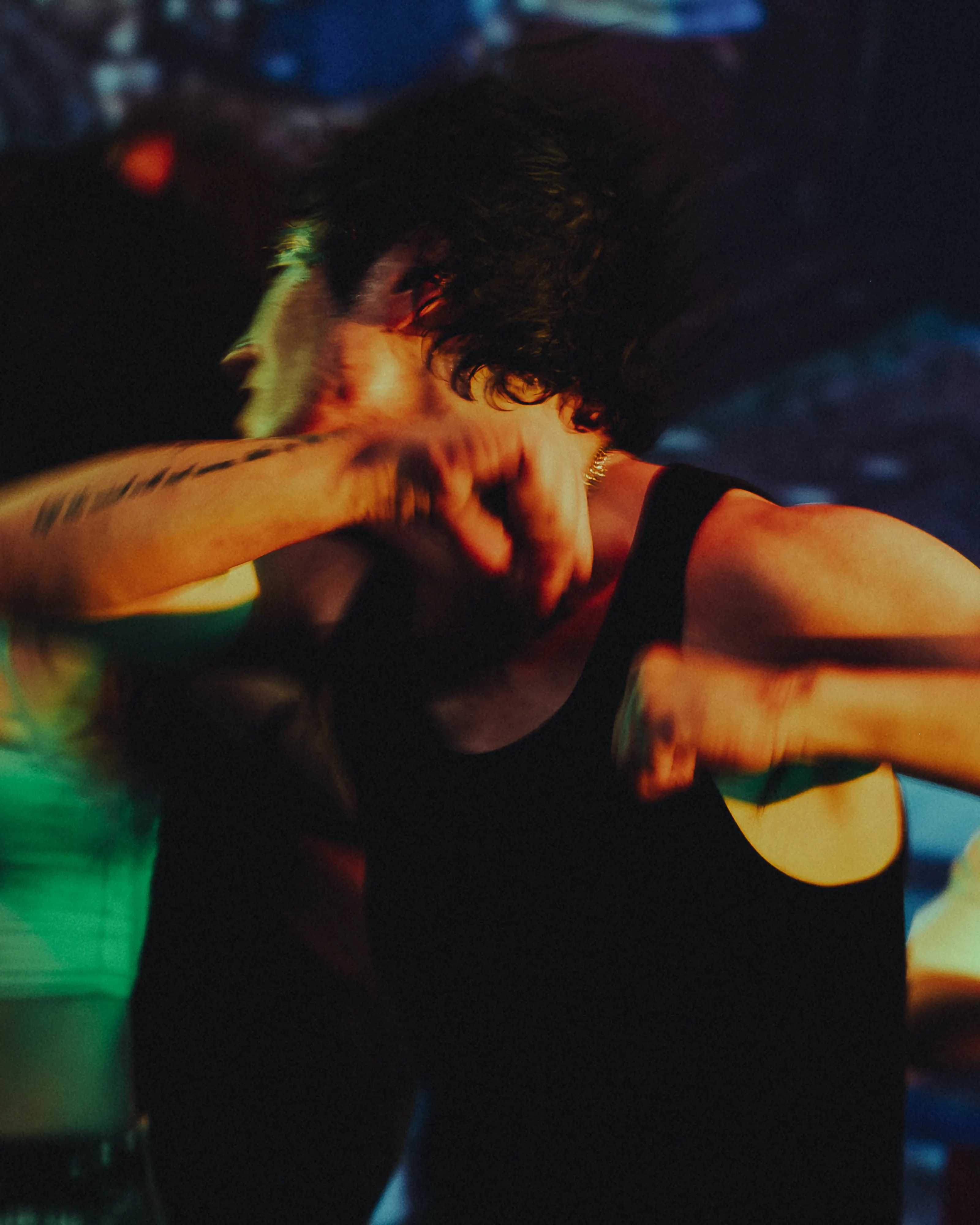 A dancer mid-swing, arm blurred across his face under club light, as shot